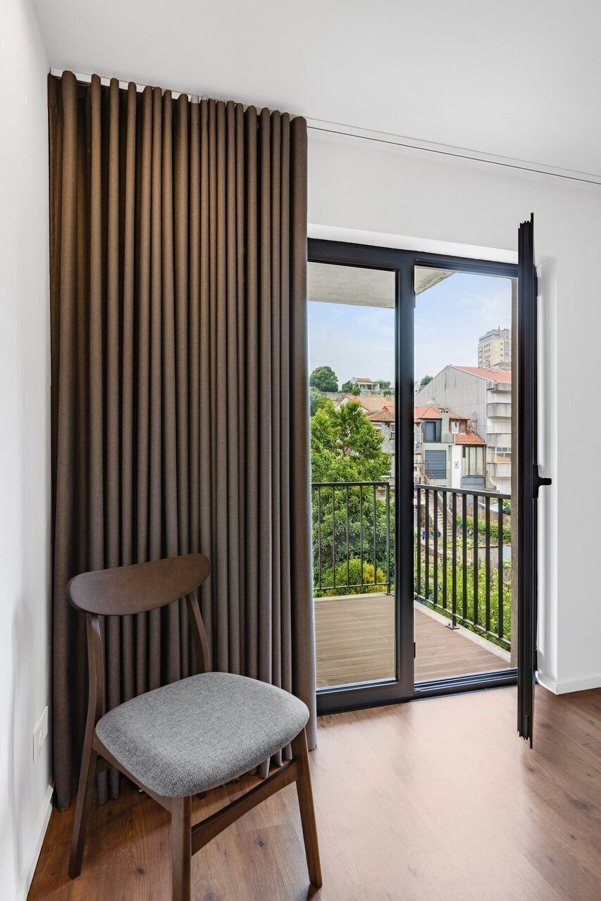 Een kamer met een schuifglazen deur naar een balkon, een stoel en een verticale jaloezie.