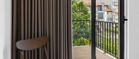 Une pièce dotée d’une porte-fenêtre coulissante donnant sur un balcon, d’une chaise et d’un store vertical.