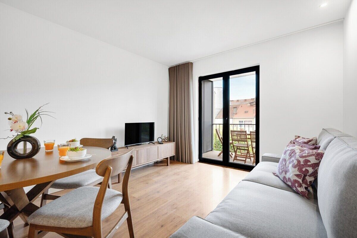 A modern living room with a dining area, a flat-screen TV, and a sofa with patterned cushions.
