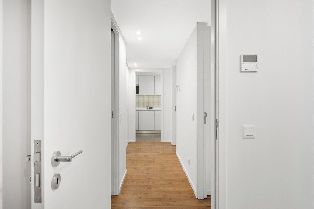 A hallway with white walls, a wooden floor, and a door with a keyhole and a lock.