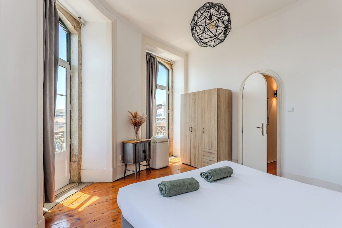 A bedroom with a bed, two towels, a desk, a radiator, and a wardrobe.