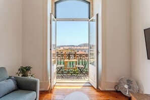 A room with a balcony, a sofa, a fan, and a view of buildings. - Bridge View Balcony, near LX Factory (Lisbon)