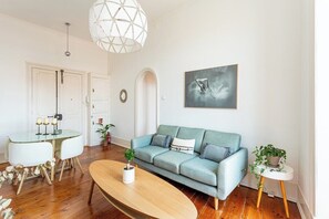 A living room with a sofa, coffee table, and dining table. - Bridge View Balcony, near LX Factory (Lisbon)