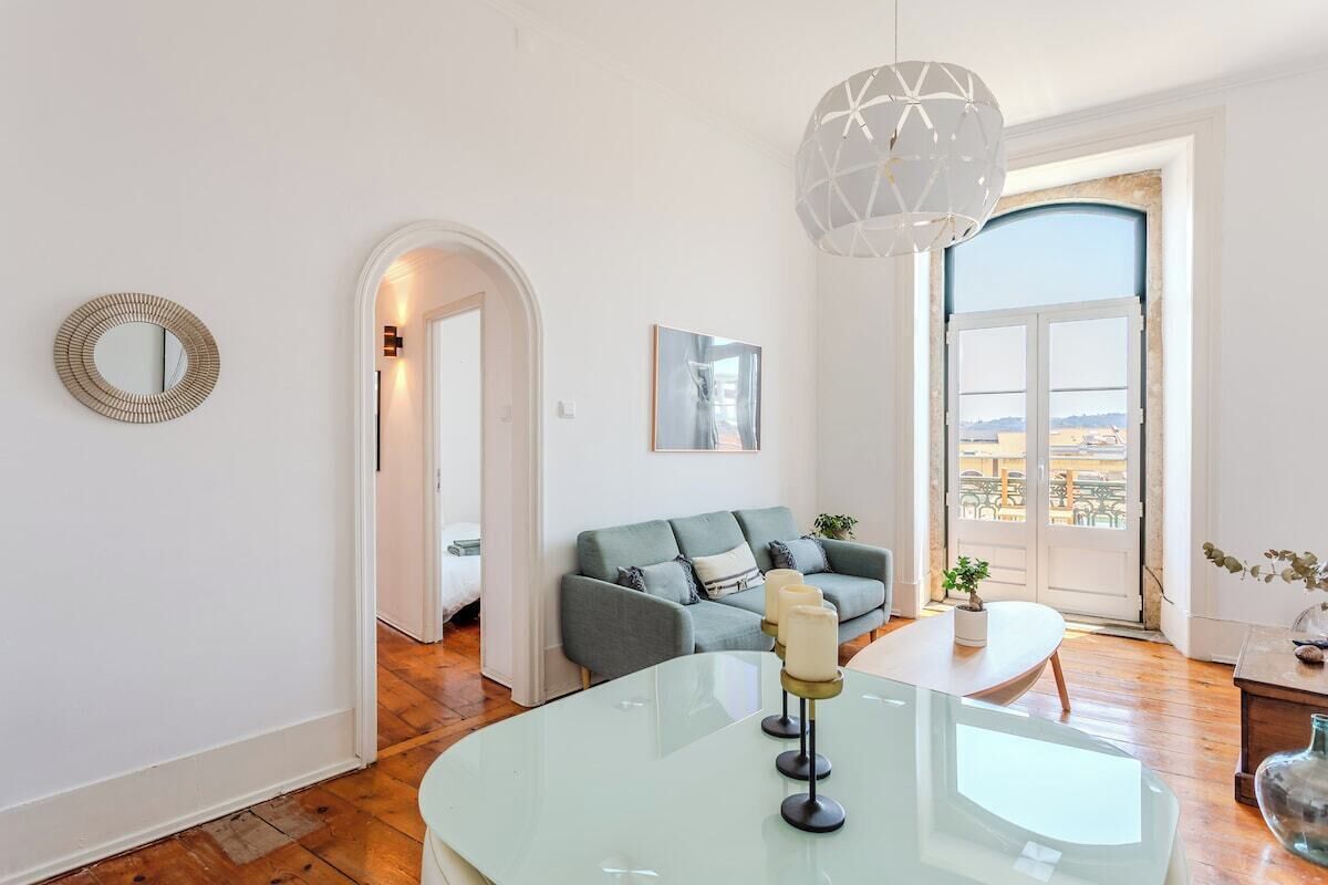 Una sala de estar moderna con una mesa de centro de vidrio, un sofá gris, un espejo redondo y un ventanal con vistas.