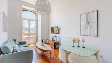 Una sala de estar moderna con un sofá, una mesa de comedor de vidrio con velas, un televisor y una obra de arte enmarcada en la pared.