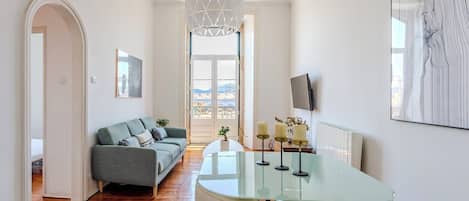 A modern living room with a glass table, a sofa, and a view through a large window.