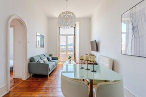 A modern living room with a glass table, a sofa, and a view through a large window. - Bridge View Balcony, near LX Factory (Lisbon)