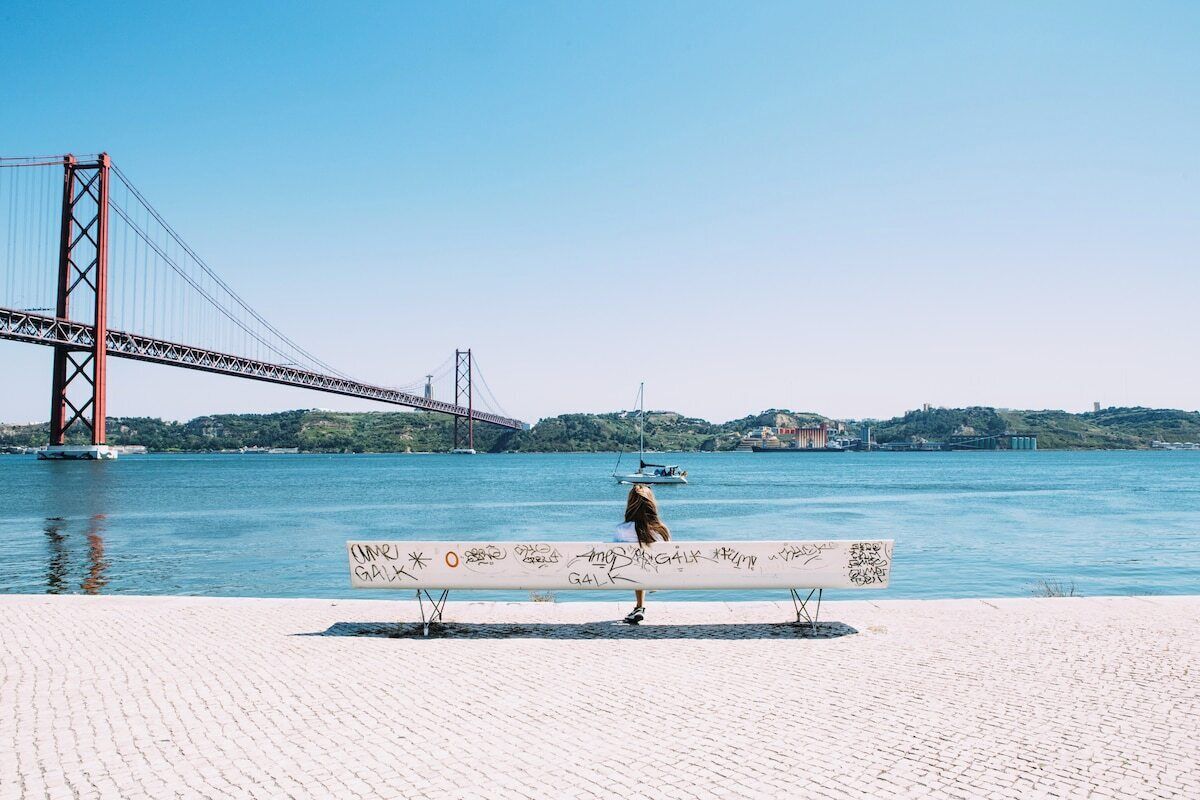 A bench by a waterfront with a bridge in the background.