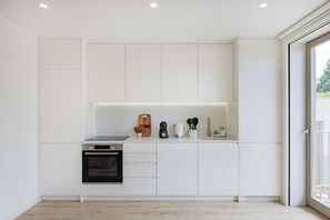 A modern kitchen with white cabinetry, a built-in oven, and a countertop with various appliances and utensils. - The Light Loft @ BoaVista Flats (Porto)