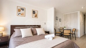 Ein Hotelzimmer mit Bett, Nachttisch, Lampe und einer kleinen Essecke mit Stühlen und Tisch.