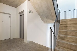 Un escalier avec une finition en béton, une porte blanche et une rampe en métal.