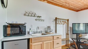 A compact kitchen with a microwave, sink, and Hisense refrigerator. There is a wooden cabinet with drawers, a shelf with jars, and a TV on a stand. - 3 Studio Suites! White River Cabin Compound (Norfork)