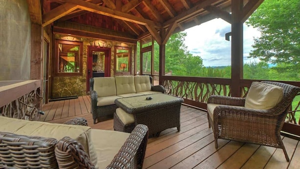 A covered outdoor area with wicker furniture, a stone wall, and a view of greenery. - The Lookout | Hot Tub + Game Room + Pet Friendly (Mineral Bluff)