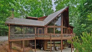 A large wooden cabin with a balcony, multiple windows, and a stone chimney. - The Lookout | Hot Tub + Game Room + Pet Friendly (Mineral Bluff)