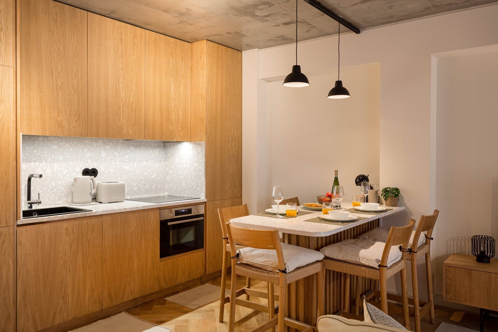 Cozinha moderna com armários de madeira, forno embutido, pia e área de jantar com mesa e cadeiras.