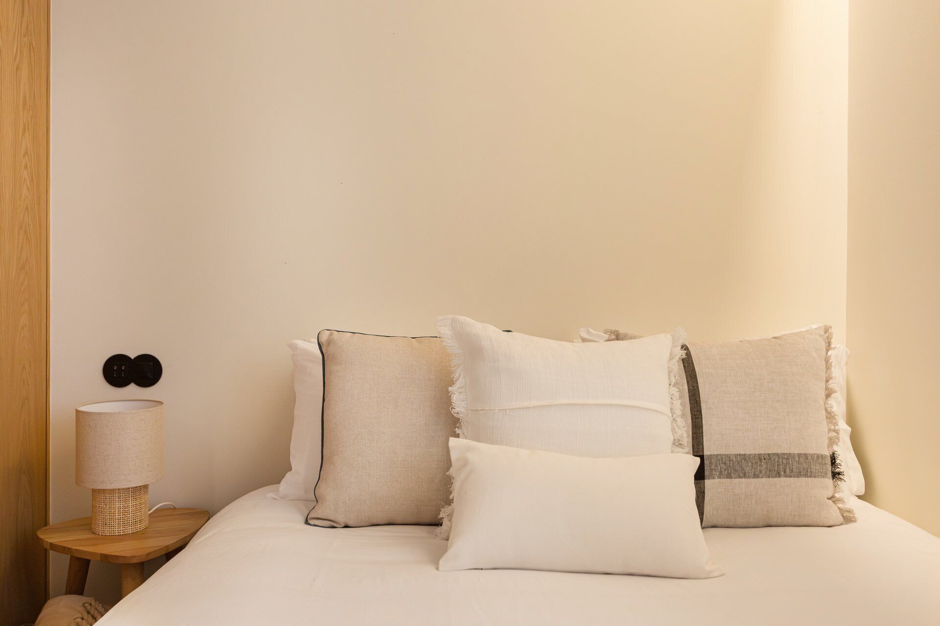 A bed with four pillows, a bedside lamp, and a wall-mounted light switch.