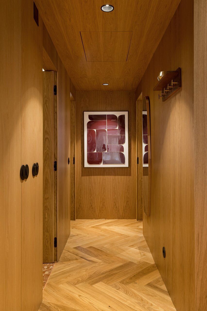 Un couloir en bois, orné d’une œuvre d’art fixée au mur, avec des portes en bois et un parquet disposé en motif chevrons.