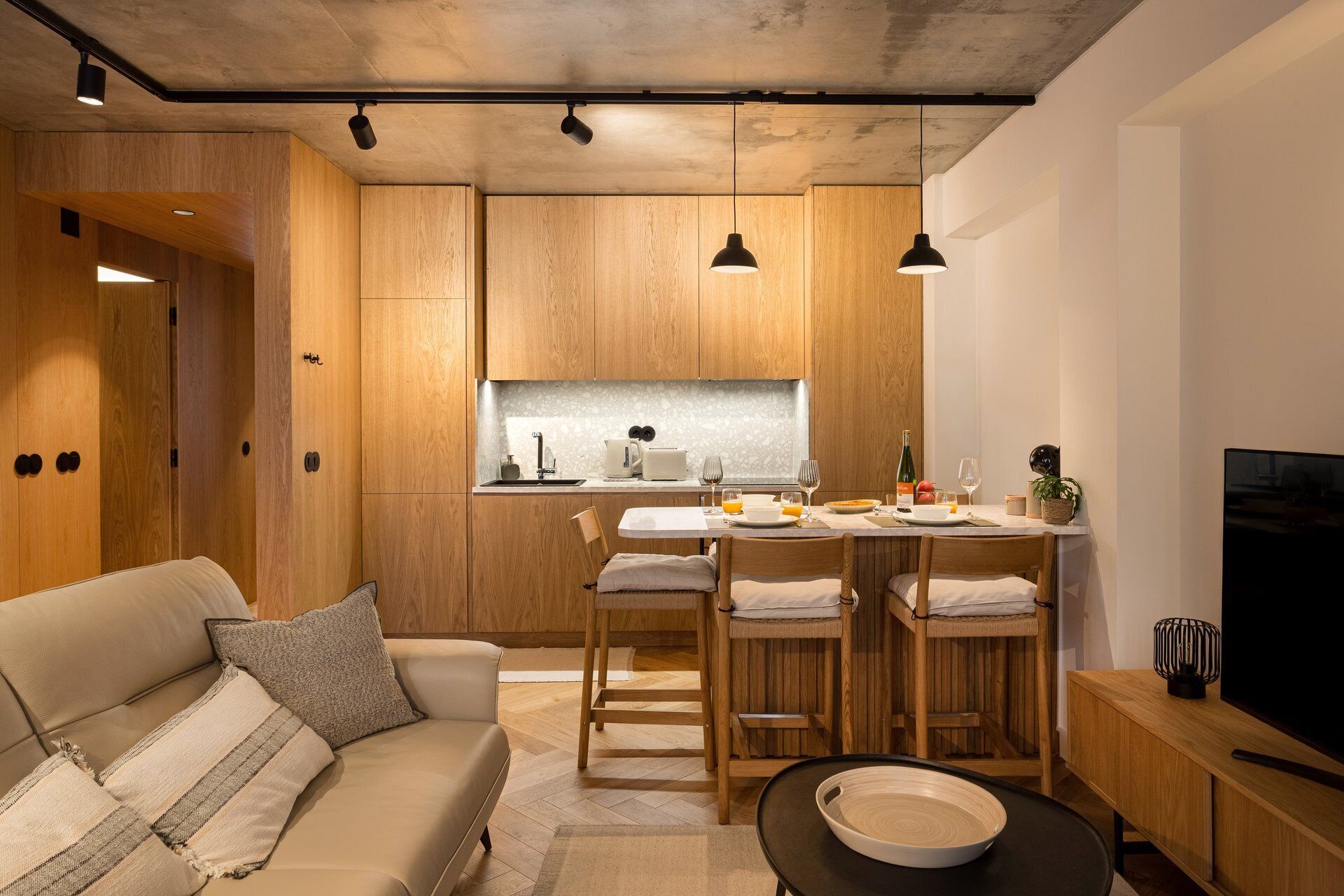 A modern kitchen with wooden cabinets, a dining area with a table and chairs, a sofa, and a television.