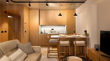 A modern kitchen with wooden cabinets, a dining area with a table and chairs, a sofa, and a television.