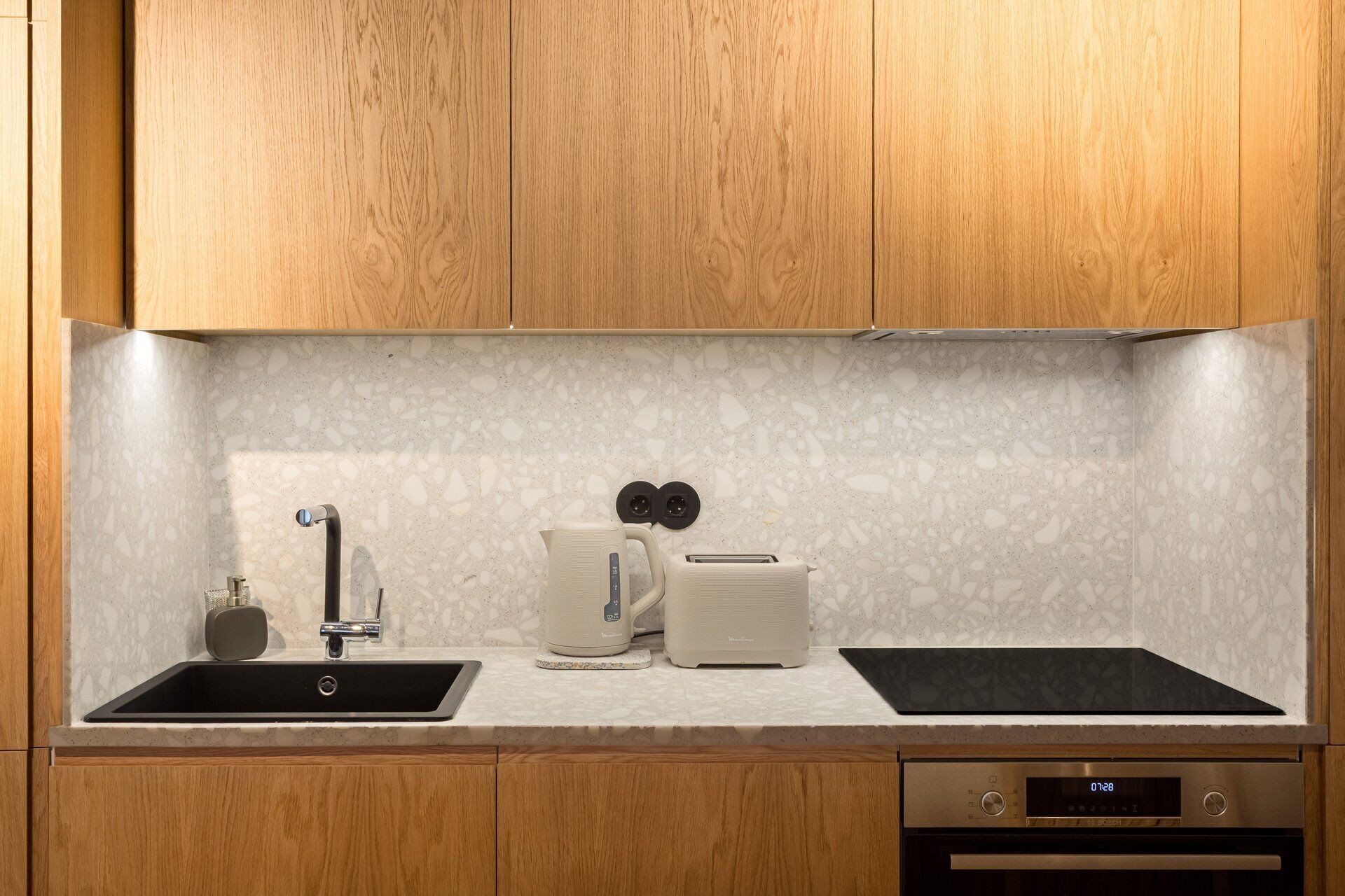 A kitchen with wooden cabinets, a granite countertop, a sink, a toaster, and an oven.