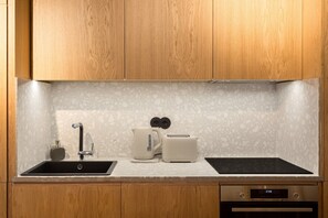 A kitchen with wooden cabinets, a granite countertop, a sink, a toaster, and an oven. - Design 2BR in Campo de Ourique (Lisbon)