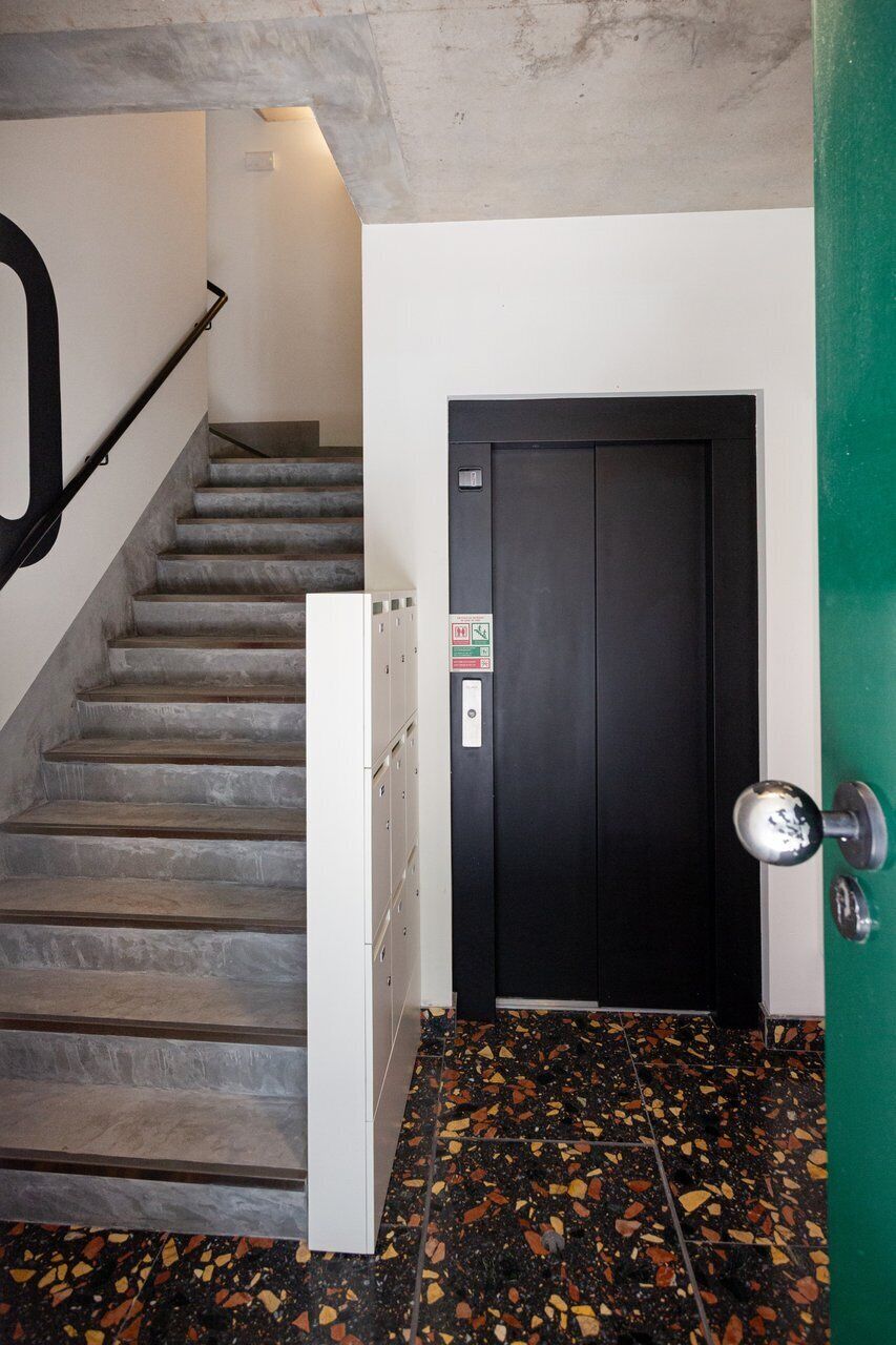 Escada que leva a uma porta com puxador de metal, um armário branco e um chão de terrazzo.