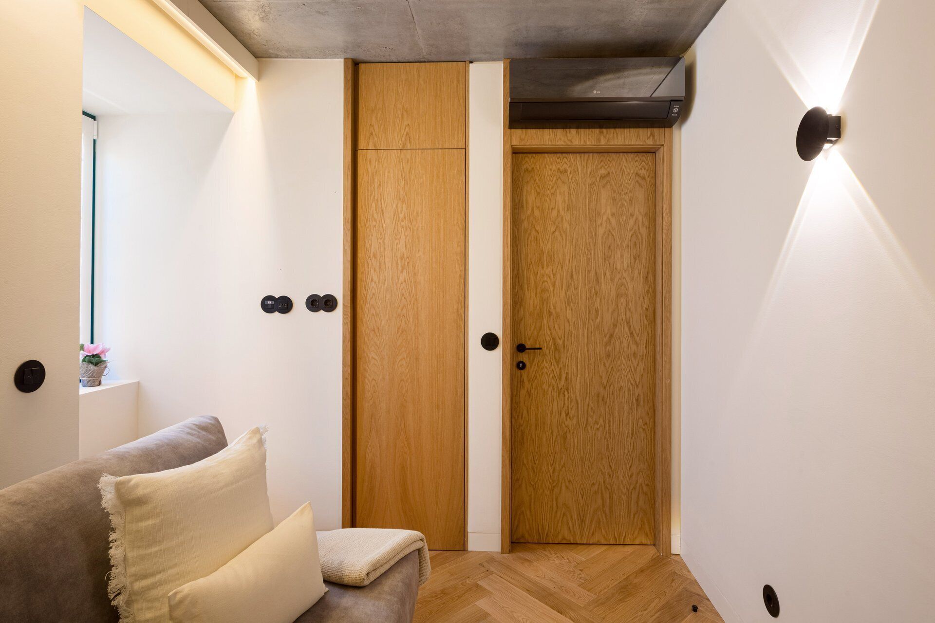 Quarto com guarda-roupa de madeira, sofá com almofadas e luminária fixada na parede.