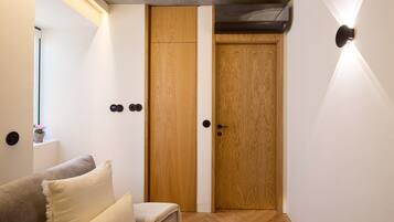Quarto com guarda-roupa de madeira, sofá com almofadas e luminária fixada na parede.