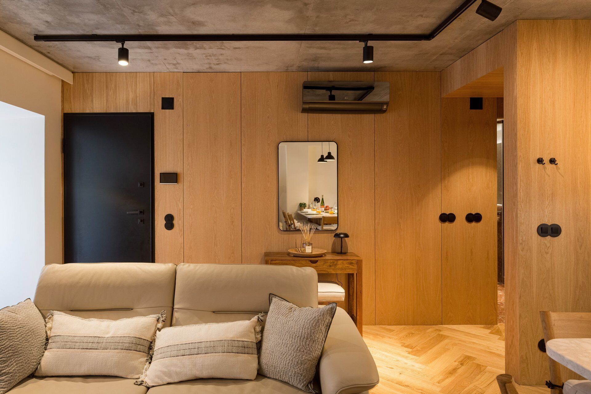 Una habitación moderna con sofá, paneles de madera, un espejo y una lámpara en el techo.