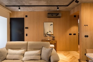 A modern room with a sofa, wooden panel walls, a mirror, and a ceiling light fixture. - Design 2BR in Campo de Ourique (Lisbon)