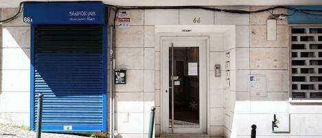 Un edificio con un acceso con persianas azules, una puerta con un letrero y el número '66' en la pared.