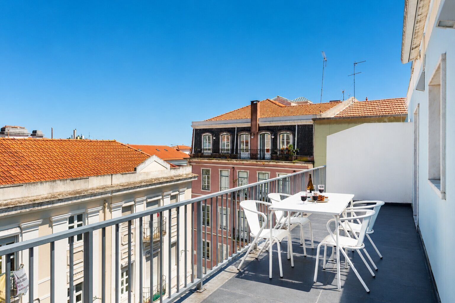 Un balcón con mesa y sillas, con vista a un paisaje urbano de tejados rojos.