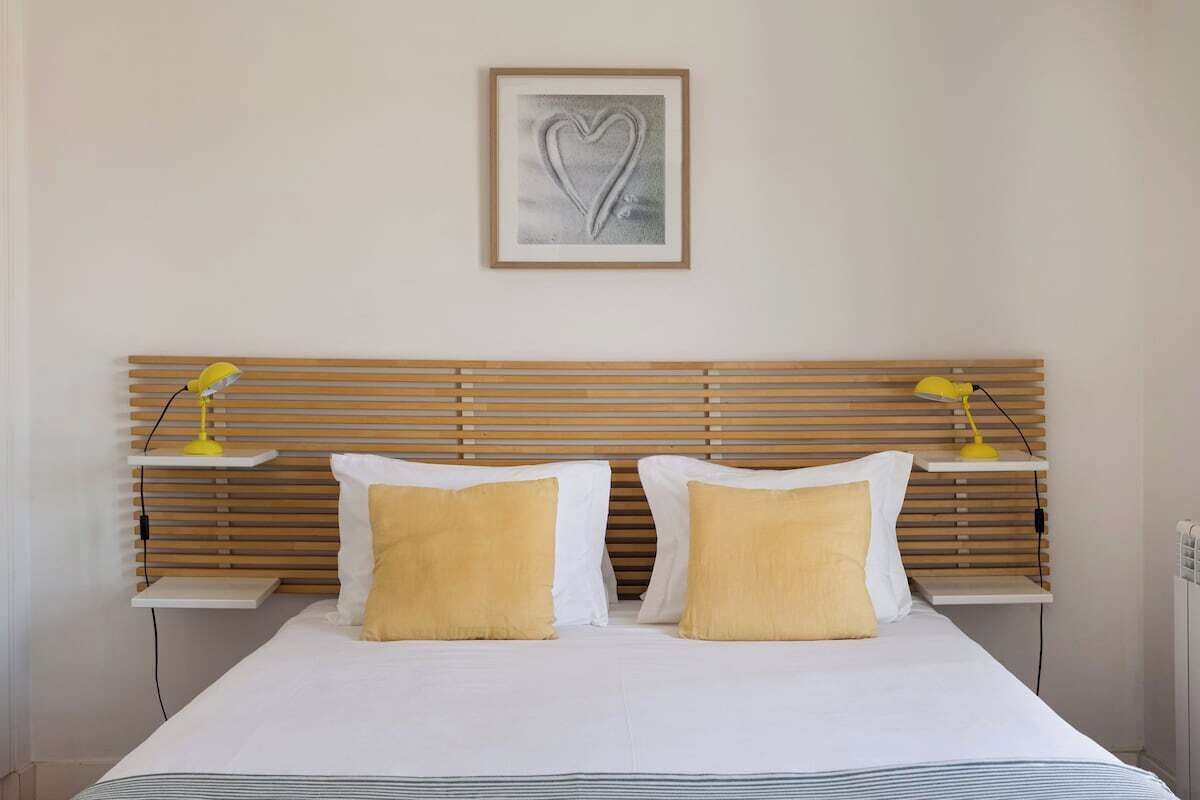 A bed with white bedding and two pillows, a wooden headboard, two bedside tables with lamps, and a framed picture on the wall.