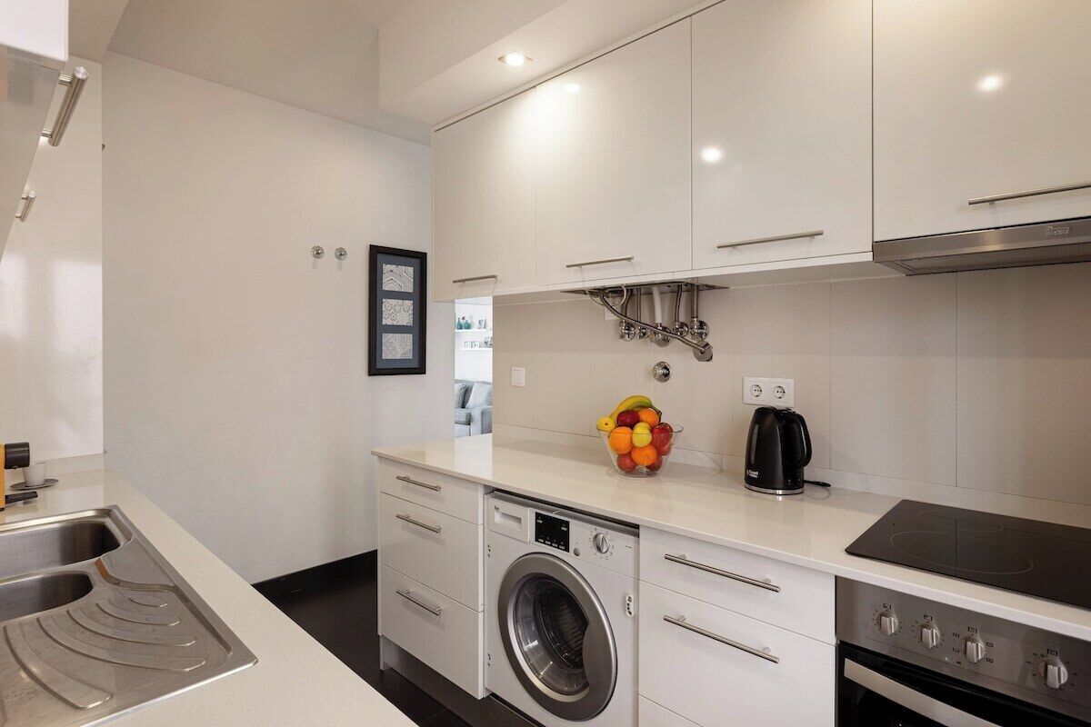 Een moderne keuken met een ingebouwde wasmachine, een koffiezetapparaat en een fruitschaal op het aanrecht.