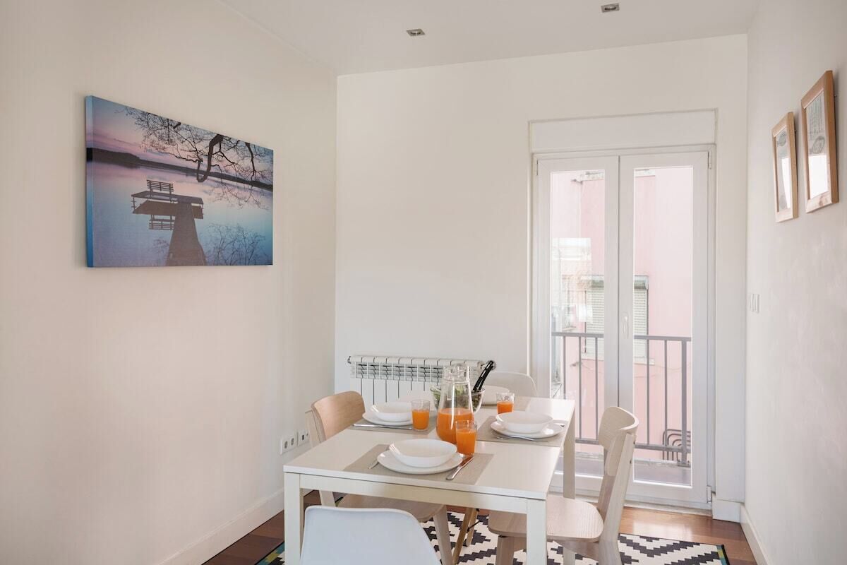 A dining area with a table set for two, a radiator, and a view of the outside balcony.