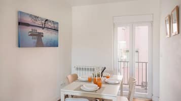 A dining area with a table set for two, a radiator, and a view of the outside balcony.
