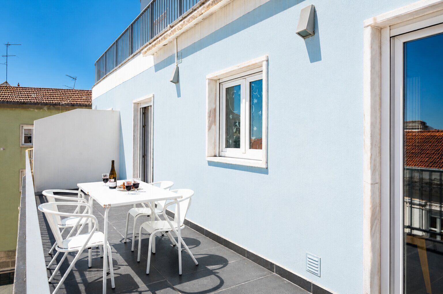 A balcony with a white table and chairs, a bottle of wine, and a glass of red wine.