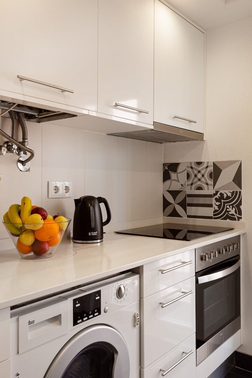 Een keuken met een wasmachine, oven en een fruitschaal met een waterkoker.