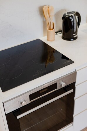A kitchen with a black induction cooktop, a stainless steel oven, and a black coffee maker on the counter. - The Morning Light @ BoaVista Flats (Porto)