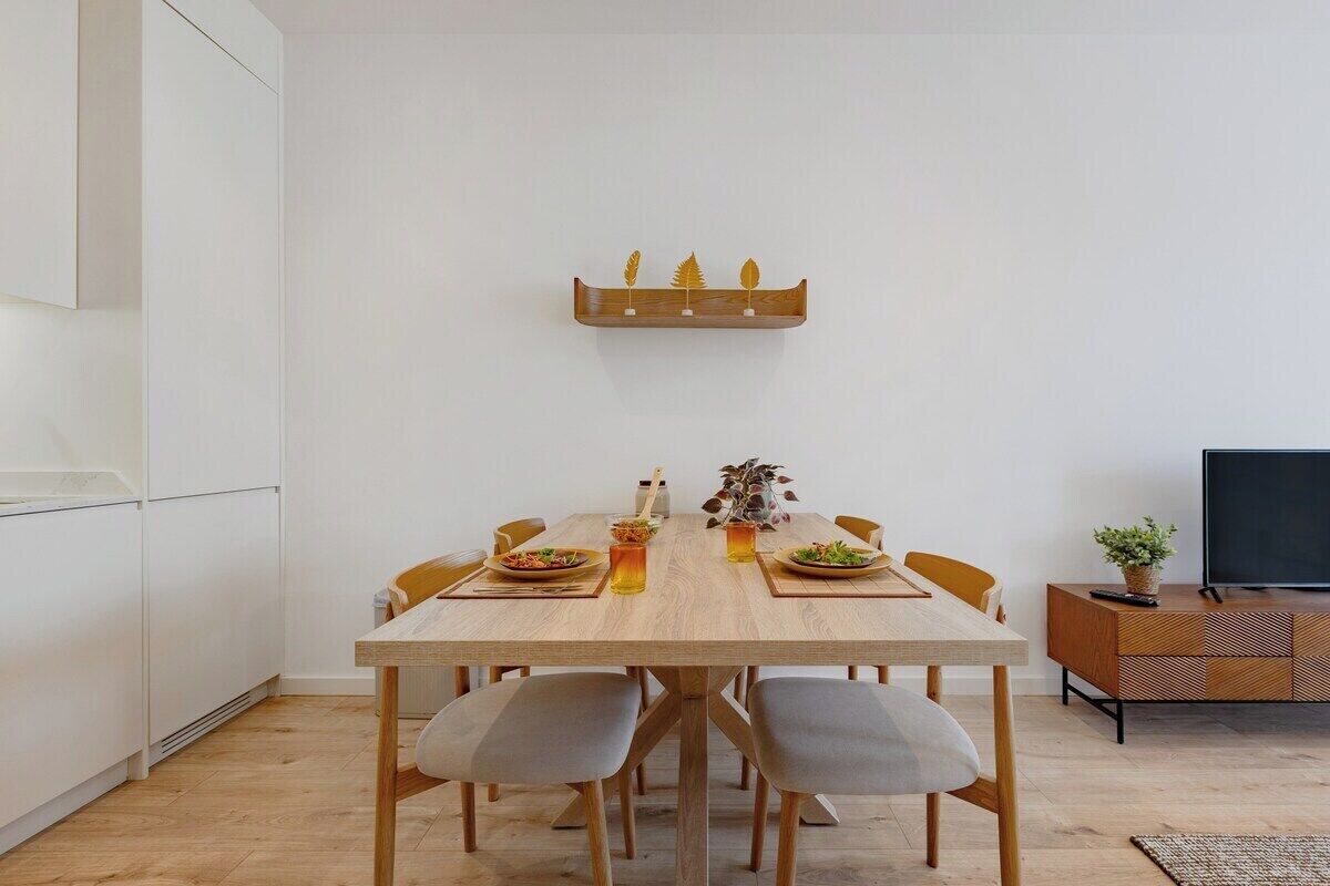 Un coin repas comprenant une table en bois, six chaises, un téléviseur et une petite étagère ornée d’objets décoratifs.