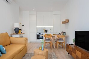 Uma sala de estar moderna com sofá, televisão, área de jantar com mesa e cadeiras, e cozinha ao fundo.