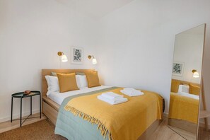Quarto de hotel com cama, mesas de cabeceira, espelho e luminárias na parede.