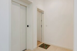 A hallway with a closed door, a doorbell, and a small rug on the floor. - The Morning Light @ BoaVista Flats (Porto)