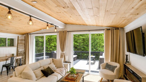 Un vaste espace de vie doté d’un plafond en bois, de grandes fenêtres, d’un canapé, d’une table basse et d’un téléviseur fixé au mur.