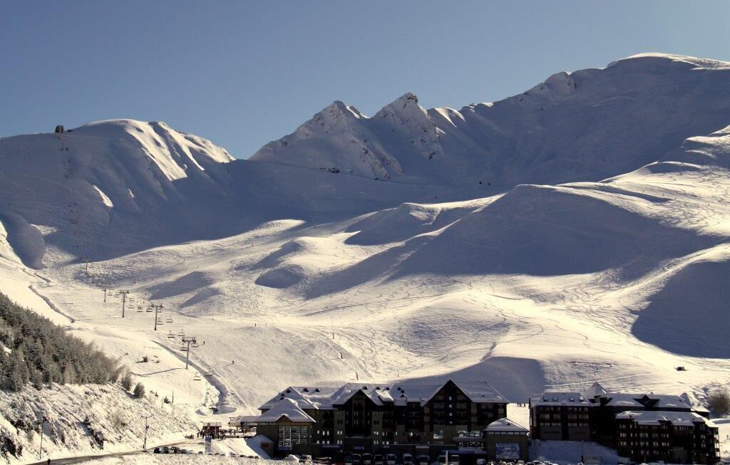 Een met sneeuw bedekte berg met skipistes, een stoeltjeslift en een rij gebouwen met sneeuwdakken.