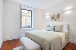 A bedroom with a bed, a window, a wall-mounted light, and a framed picture. - 1BR with Private Patio | Porto Urban Flats (Porto)