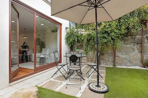 A patio with a table and chairs, a hanging umbrella, and a glass door leading to an interior space. - 1BR with Private Patio | Porto Urban Flats (Porto)
