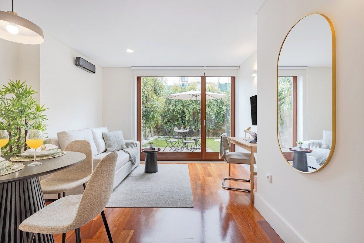 Un salon moderne avec un coin repas, de grandes portes-fenêtres coulissantes donnant sur un jardin et un grand miroir rond accroché au mur.