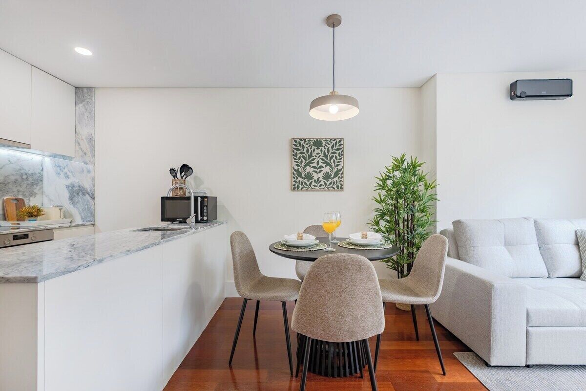 Une cuisine moderne dotée d’un plan de travail en marbre, un coin repas avec une table ronde et des chaises, et un salon avec un canapé.
