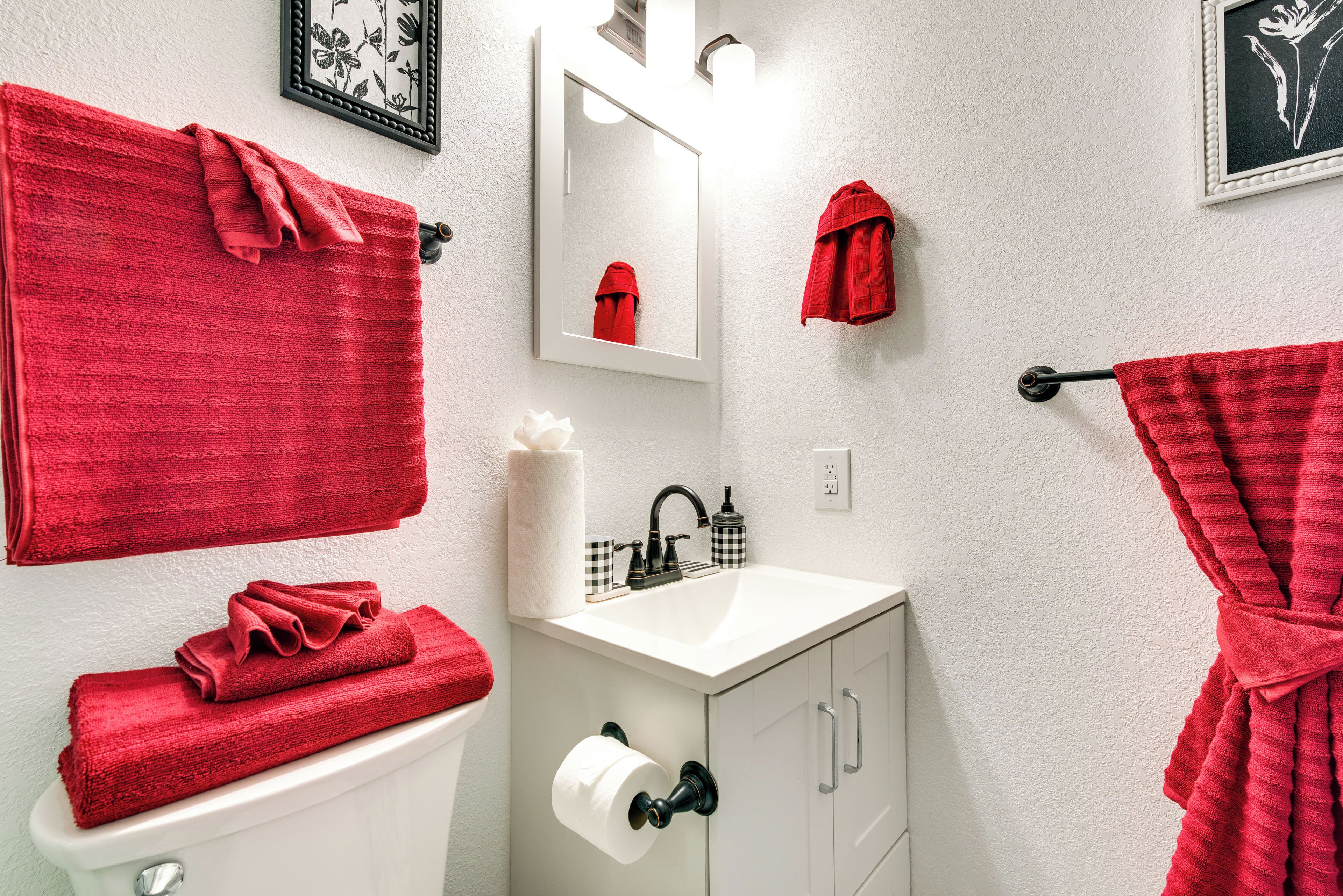 Ein Badezimmer mit einem weißen Waschbecken, einer Toilette und einem Spiegel. Rote Handtücher hängen an der Wand und ein roter Bademantel hängt an einem Haken.